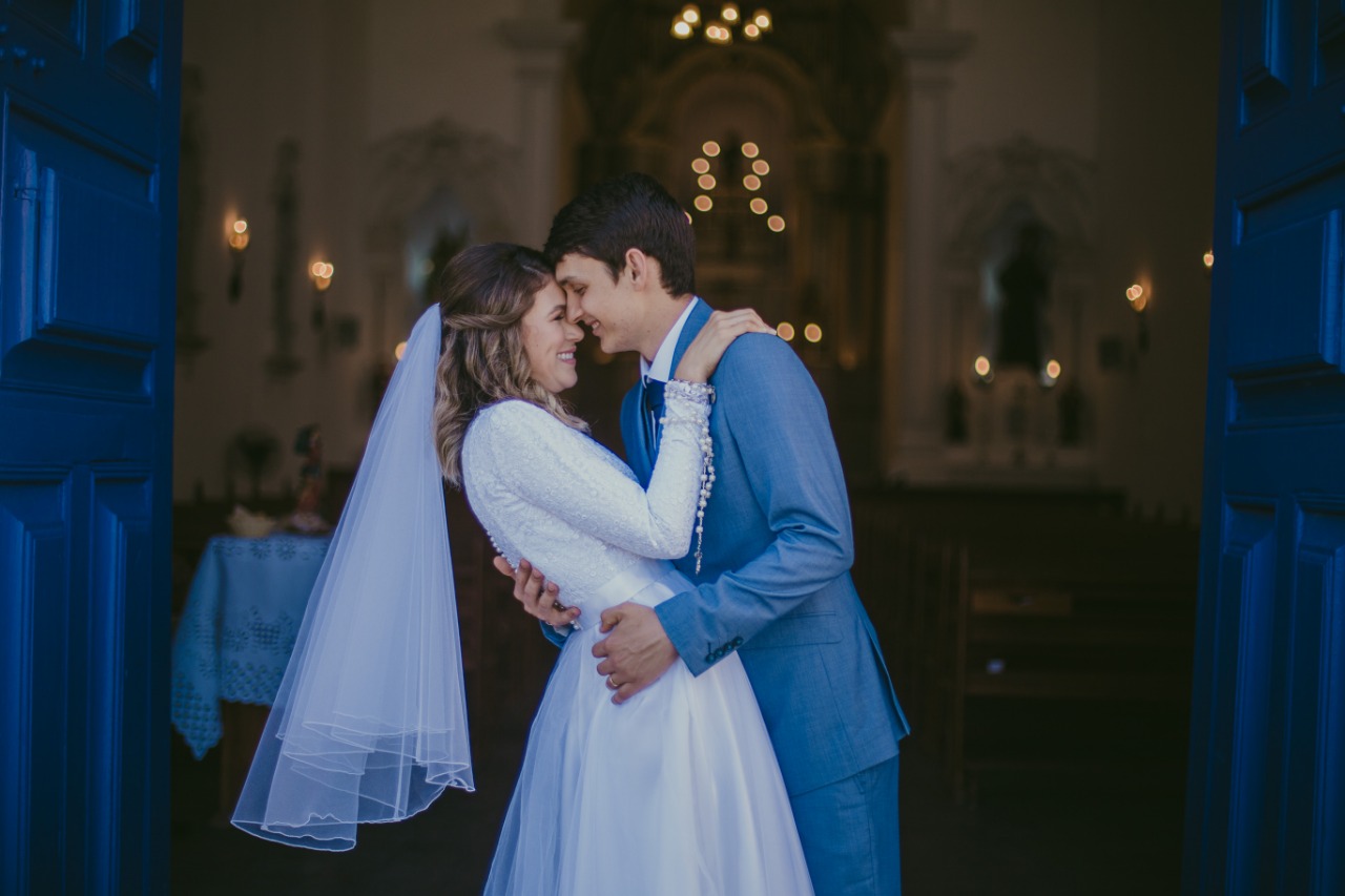 Noivos sorridentes em um abraço carinhoso dentro da igreja.