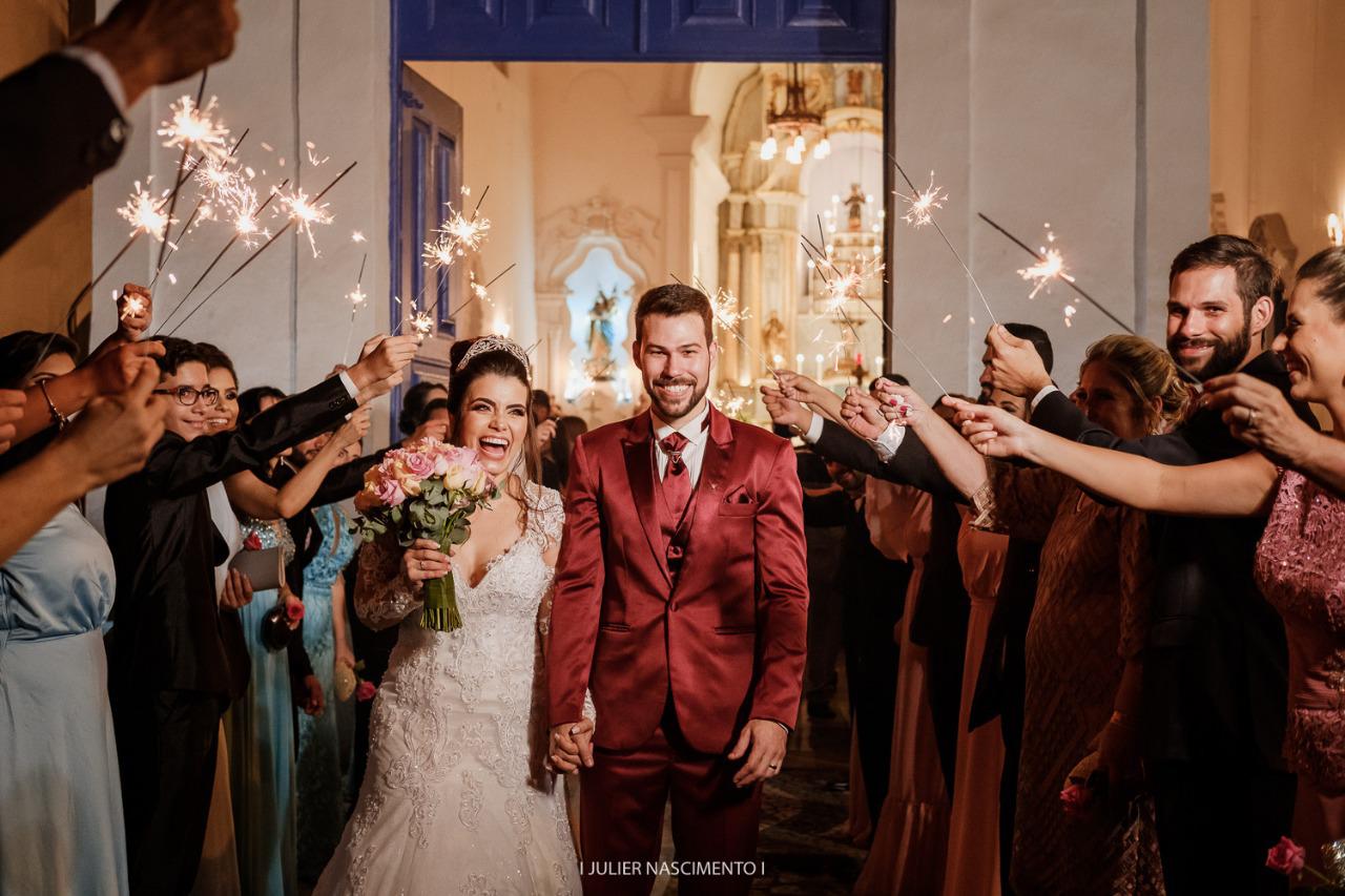 Noivos sorridentes caminhando pelo corredor de sparklers na saída da cerimônia de casamento.